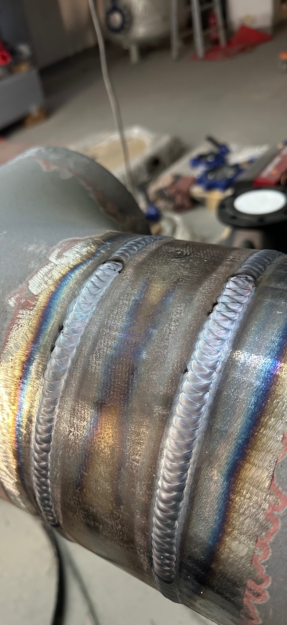 Szczegółowe zbliżenie na spawany element z widocznymi, precyzyjnymi ściegami spawalniczymi i charakterystycznymi przebarwieniami termicznymi na metalu.