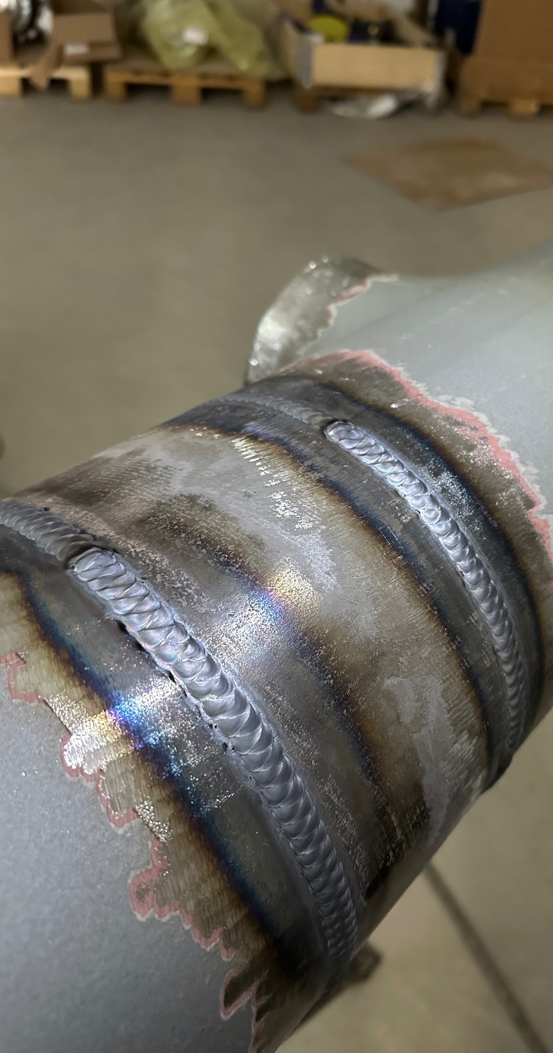 Szlifowana, spawana rura z widocznymi śladami obróbki, ukazująca precyzję wykonania. Spawy układają się w równomierne, estetyczne wzory. W tle widoczne elementy magazynu.