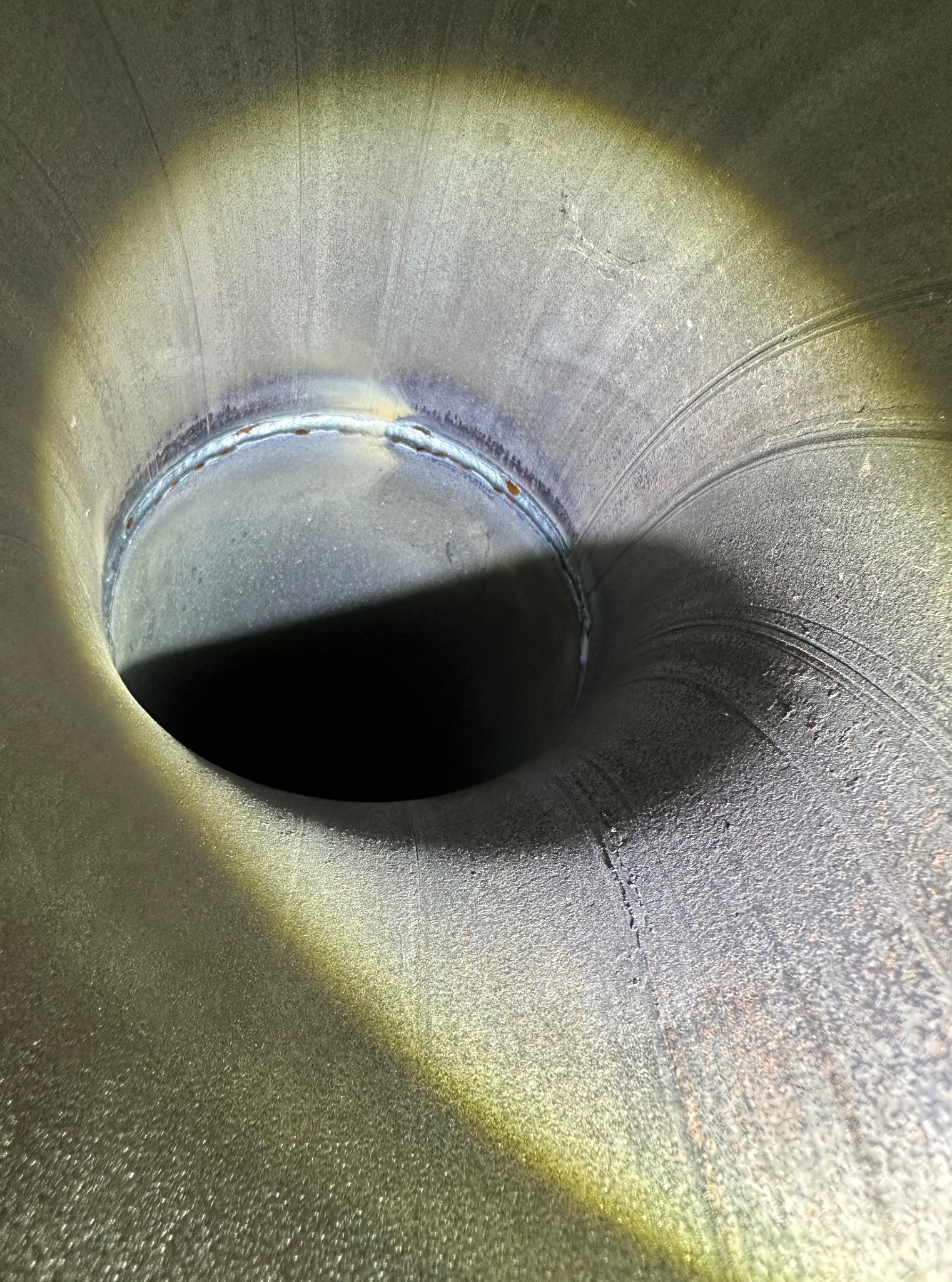 Wnętrze metalowego, spawane elementu rurowego o nieregularnym kształcie, oświetlone punktowo, ukazujące precyzyjne łączenie i strukturę materiału.