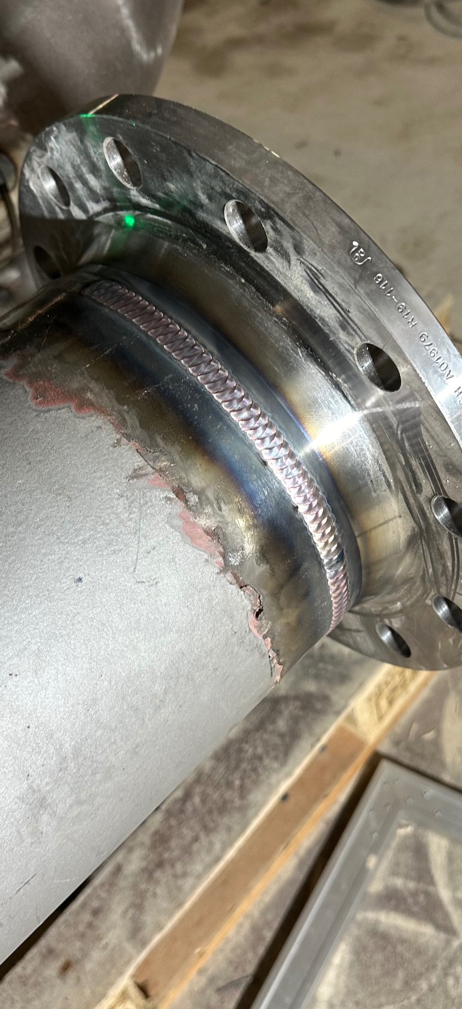 Precyzyjne spawy łączące rurę ze stalowym kołnierzem, widoczne ślady obróbki i laserowy wskaźnik. Detal spoiny i mocowania.