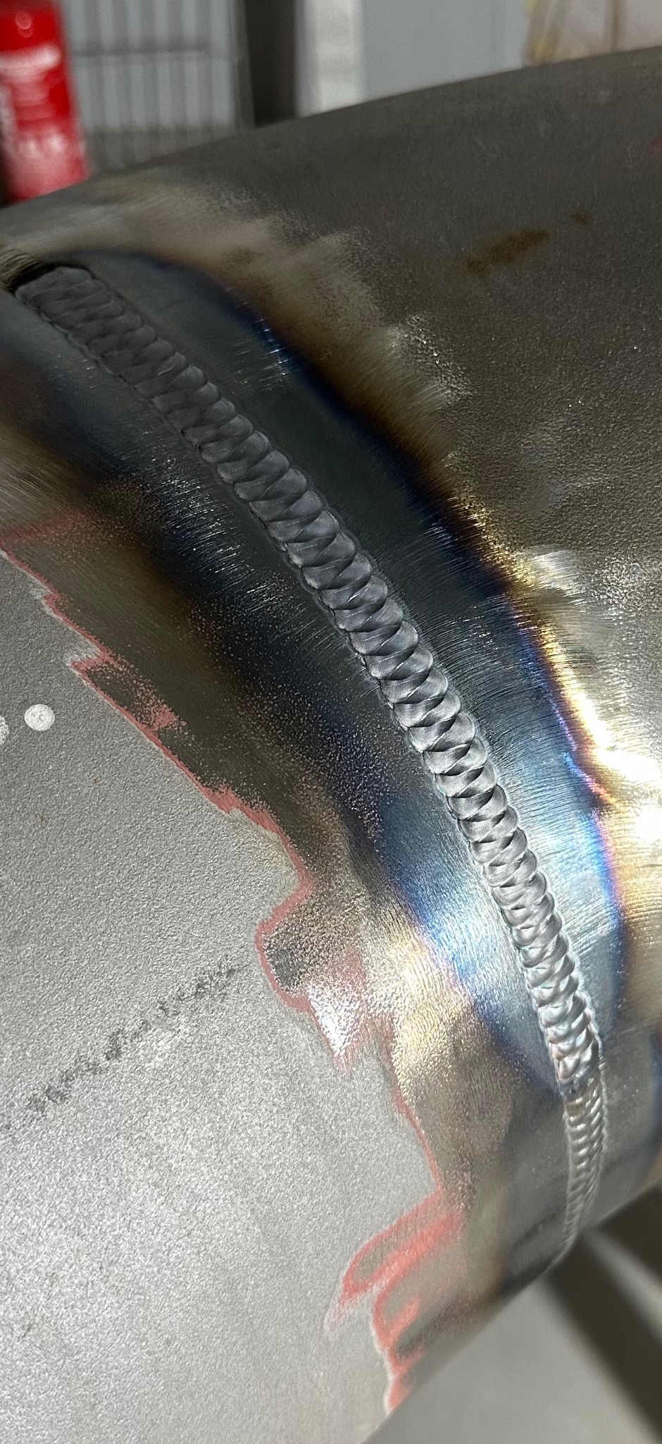 Szlifowany spaw na metalowej rurze, widoczne tęczowe przebarwienia termiczne i ślady po szlifowaniu. Precyzyjne łączenie elementów, zbliżenie na detal spoiny.