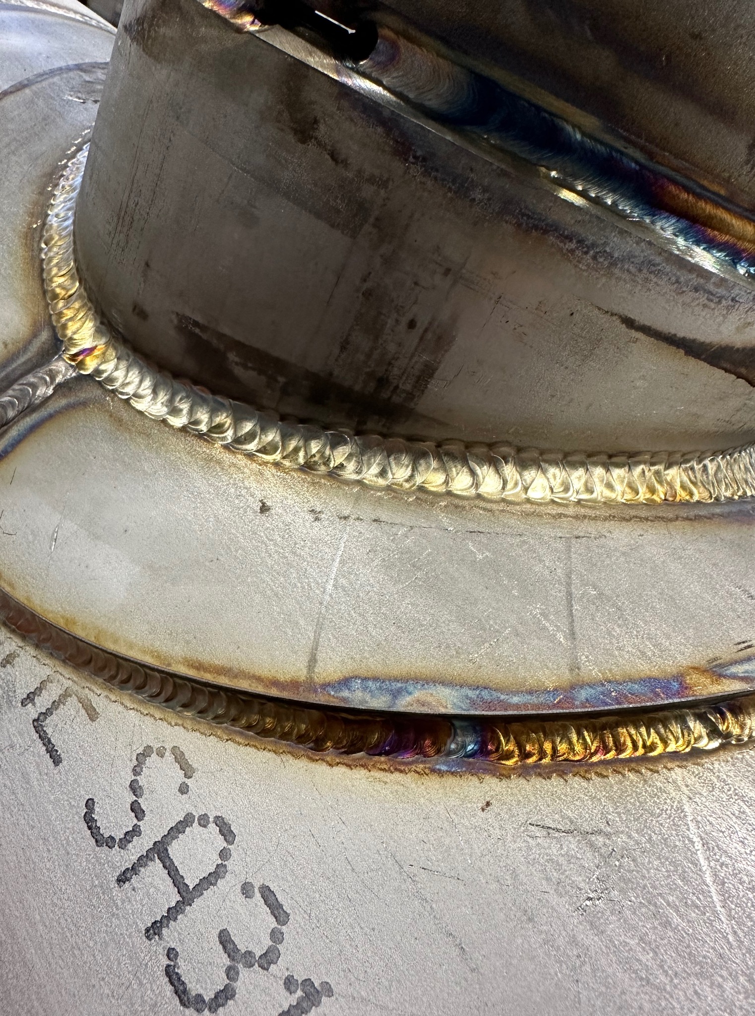 Szczegółowe zbliżenie na spaw, ukazujące precyzyjne łączenie metalowych elementów. Widoczne ślady po spawaniu i oznaczenia na powierzchni.