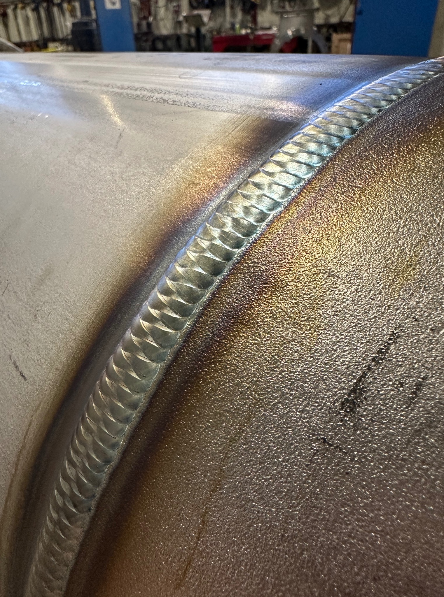 Detalista widok spoiny na metalowej rurze, ukazujący precyzyjne łączenie z opalizującymi przebarwieniami termicznymi. Widoczne ślady obróbki.