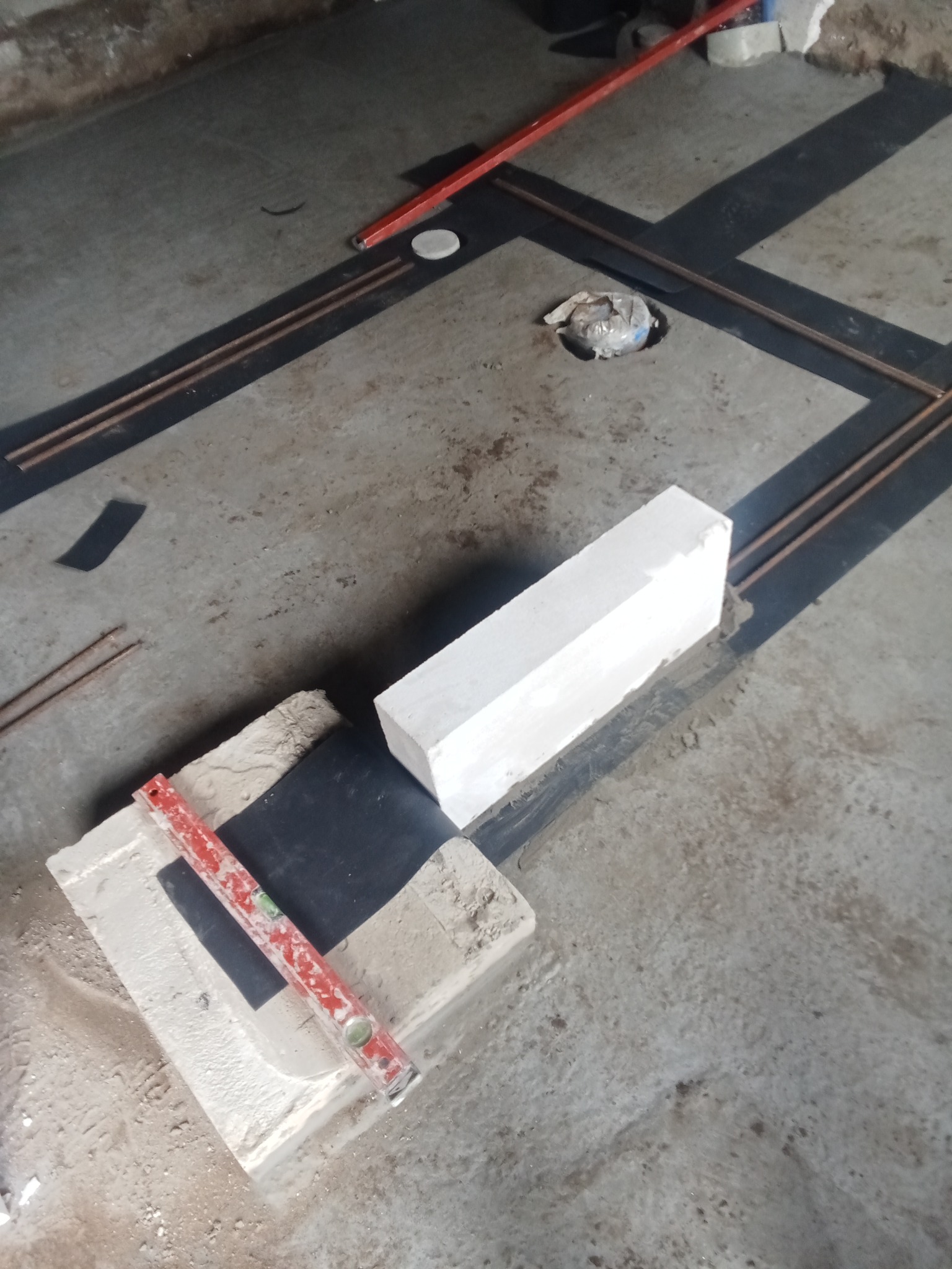 Wznoszenie muru z bloczków, poziomica na bloku, zbrojenie w posadzce. Przygotowania do murowania ścian z betonu komórkowego. Widok z góry.