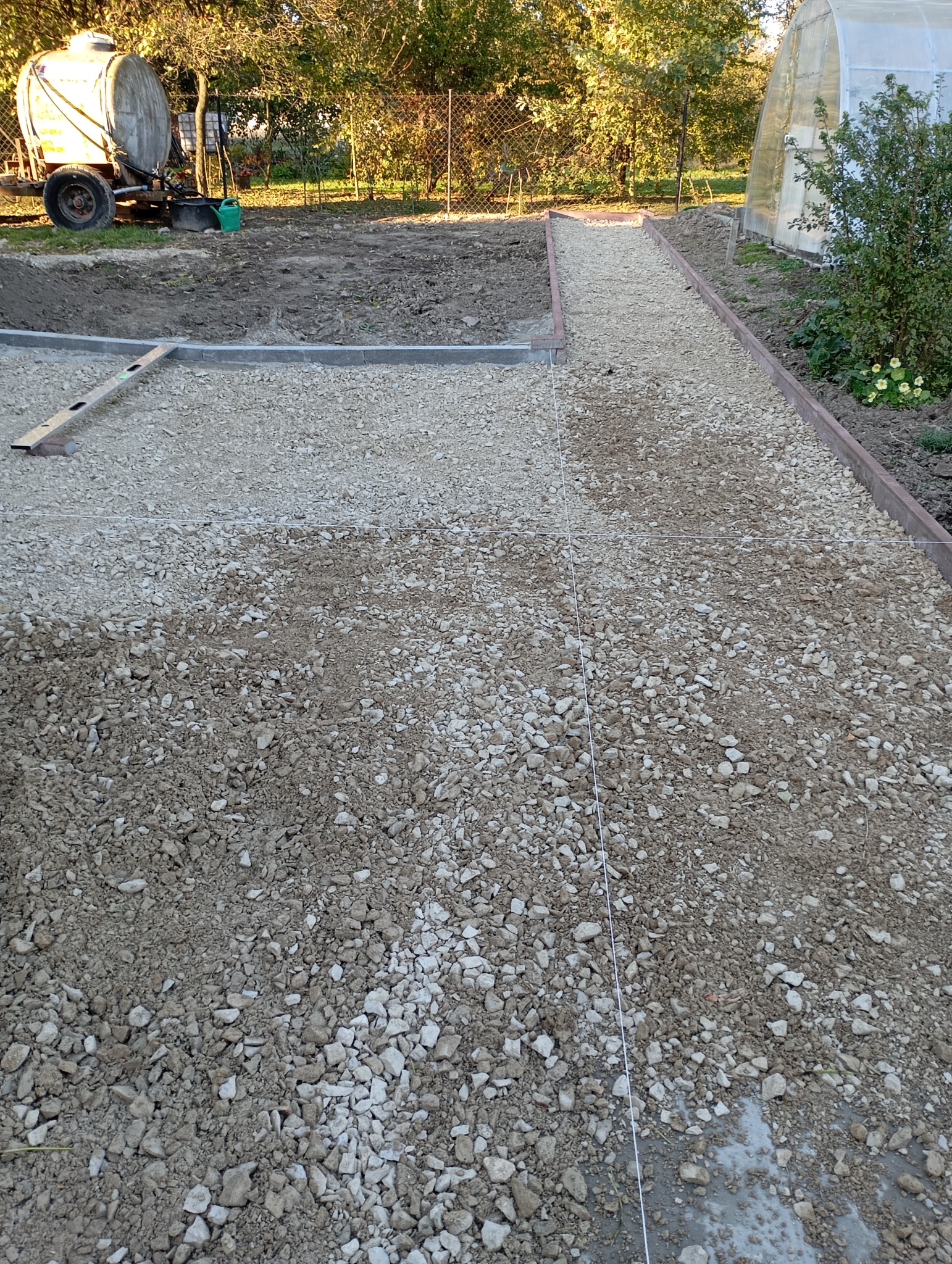 Wyrównany teren pod ścieżkę z podsypką żwirową, widoczne obrzeża, sznurek wyznaczający kierunek i poziom. W tle teren zielony.