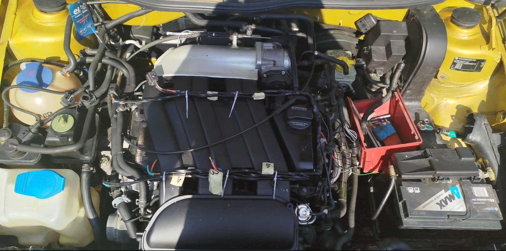 Silnik żółtego samochodu z widocznymi elementami po naprawie: nowa bateria, przewody zabezpieczone opaskami, etykiety na przewodach. Widok z góry.