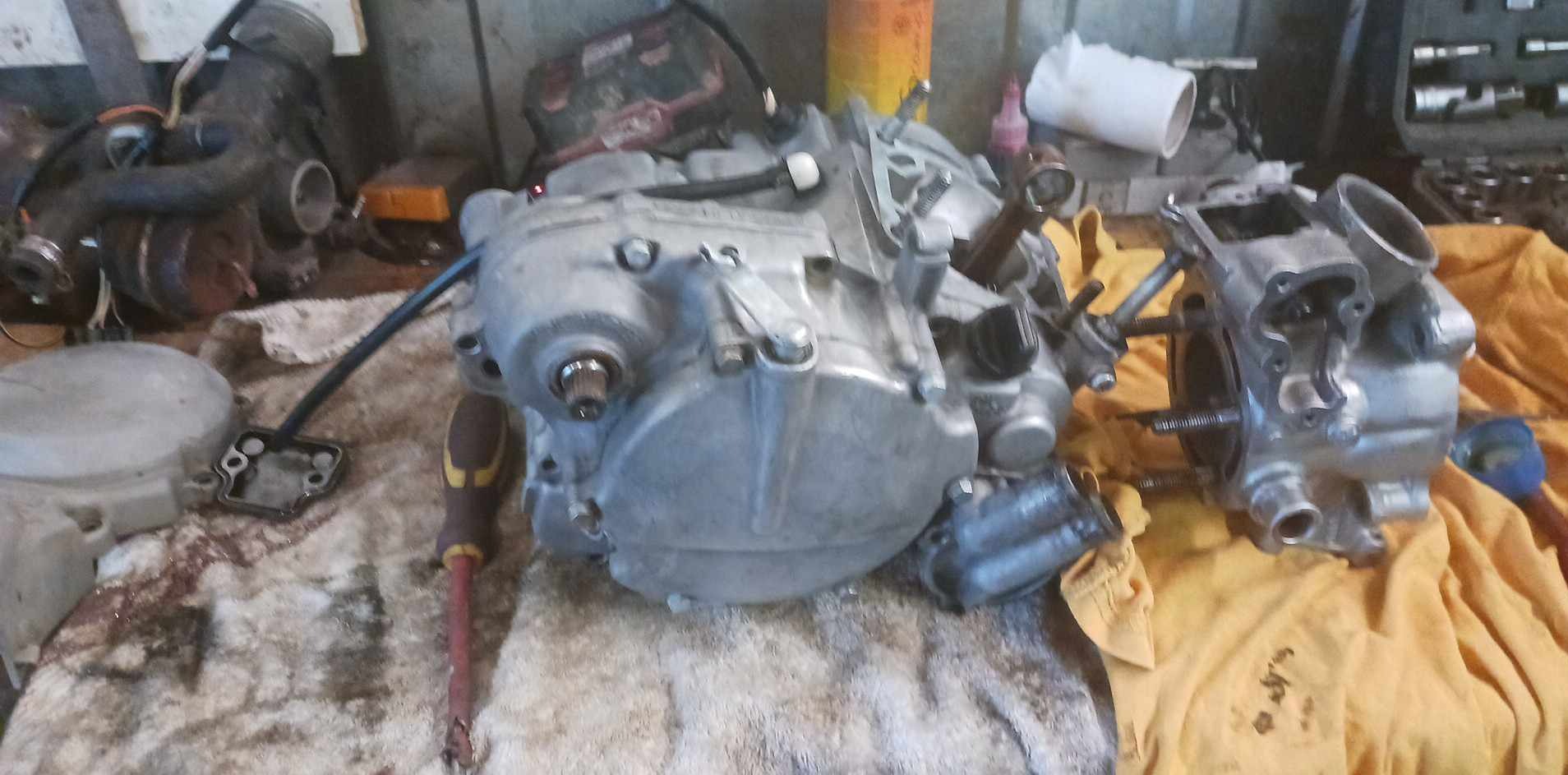 Rozłożony silnik motocyklowy na stole warsztatowym z narzędziami, widoczne elementy silnika i osprzęt. Etap naprawy lub przeglądu.