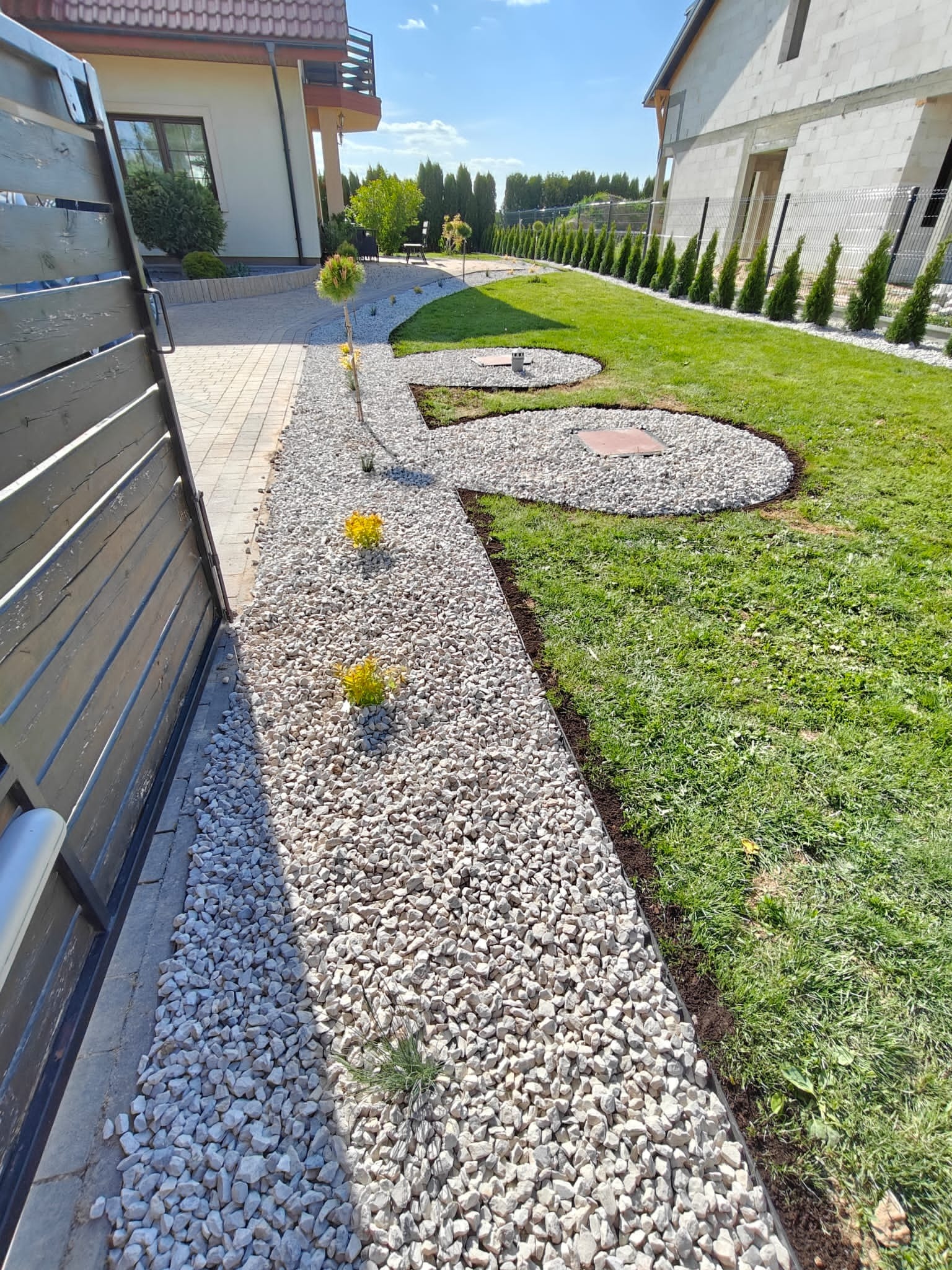 Ogród po metamorfozie w Krasnystawie: białe kamienie, rabaty z roślinami, równo przystrzyżony trawnik i szpaler iglaków. Estetyczny i zadbany.