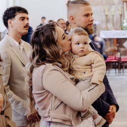 Usługi Kozłowski - Matka całuje dziecko w kościele podczas uroczystości. W tle widoczni inni goście, świece i dekoracje kwiatowe. Ujęcie z bliska, naturalne światło.