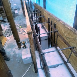 Waszka - Zbrojenie fundamentów z użyciem bloczków betonowych i stalowych prętów, widoczne szalunki z desek i narzędzia budowlane. Etap budowy domu.