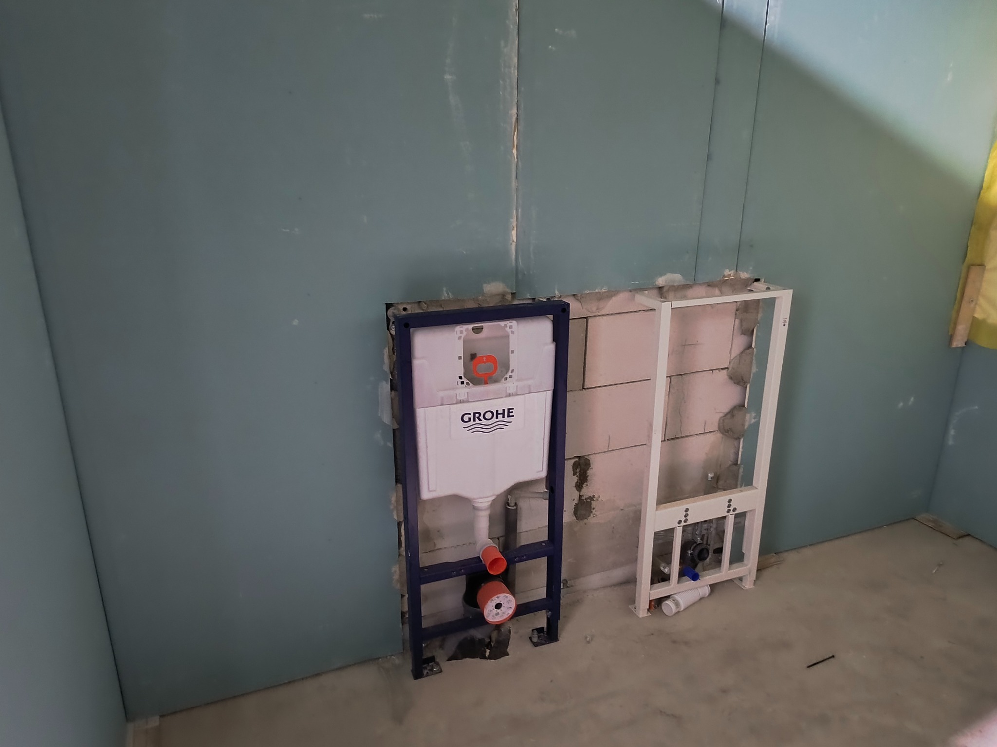 Stelaż podtynkowy Grohe zamontowany przy ścianie z płyty karton gips, widoczne elementy instalacji hydraulicznej. Surowy stan, przygotowanie do wykończenia.