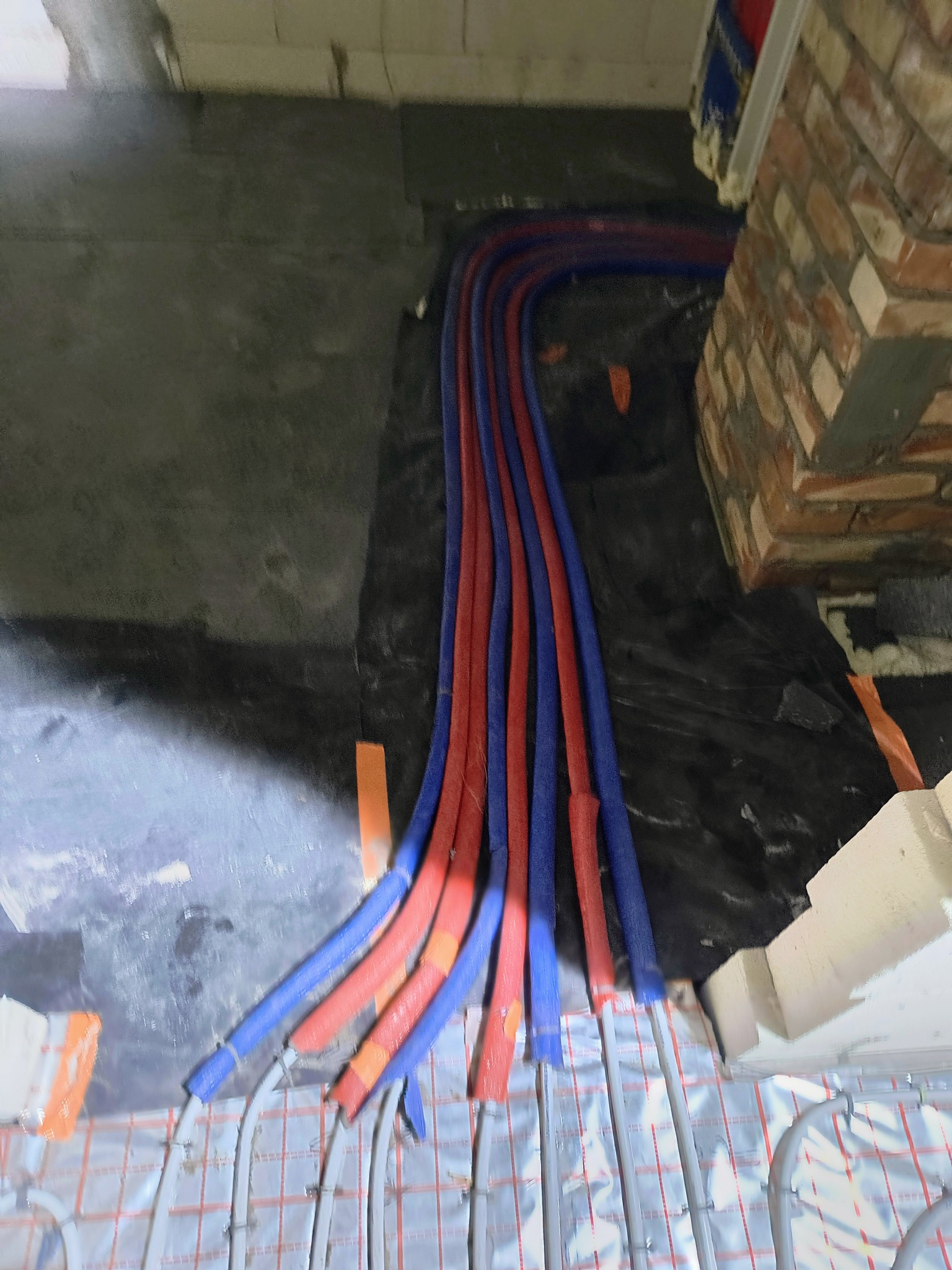 Instalacja ogrzewania podłogowego z rurami w izolacji czerwono-niebieskiej, ułożona na folii z rastrem, widok z góry, etap prac przed wylewką.