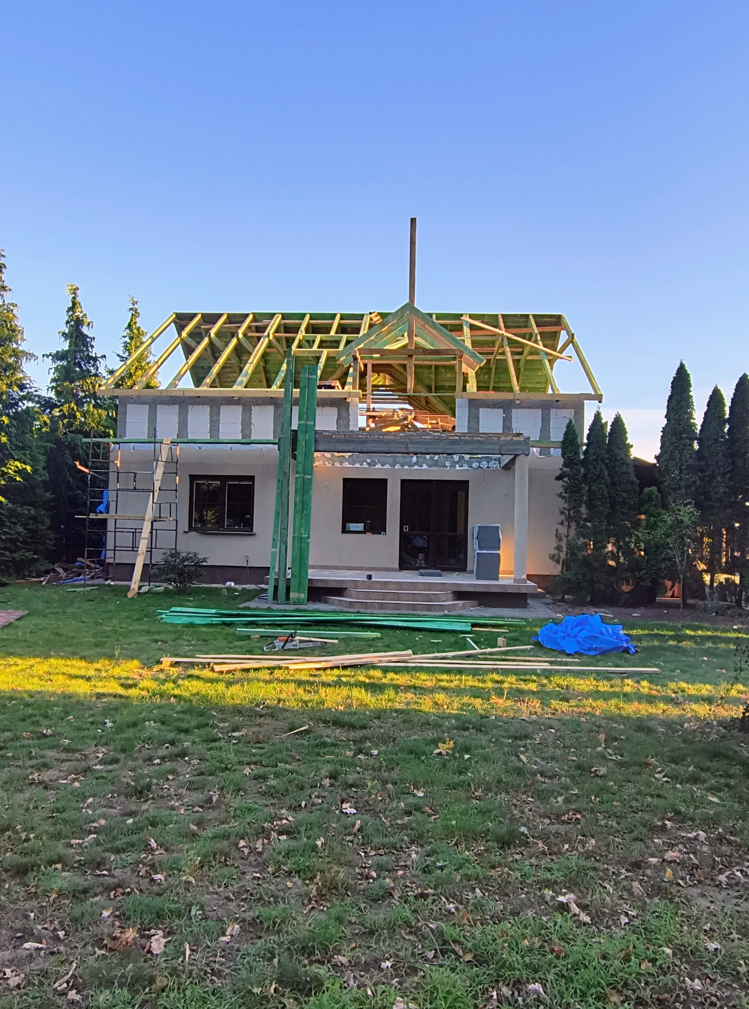 Budowa domu jednorodzinnego w Siennie: widok na budynek w trakcie wznoszenia konstrukcji dachu, z widocznymi elementami drewnianymi i rusztowaniem.