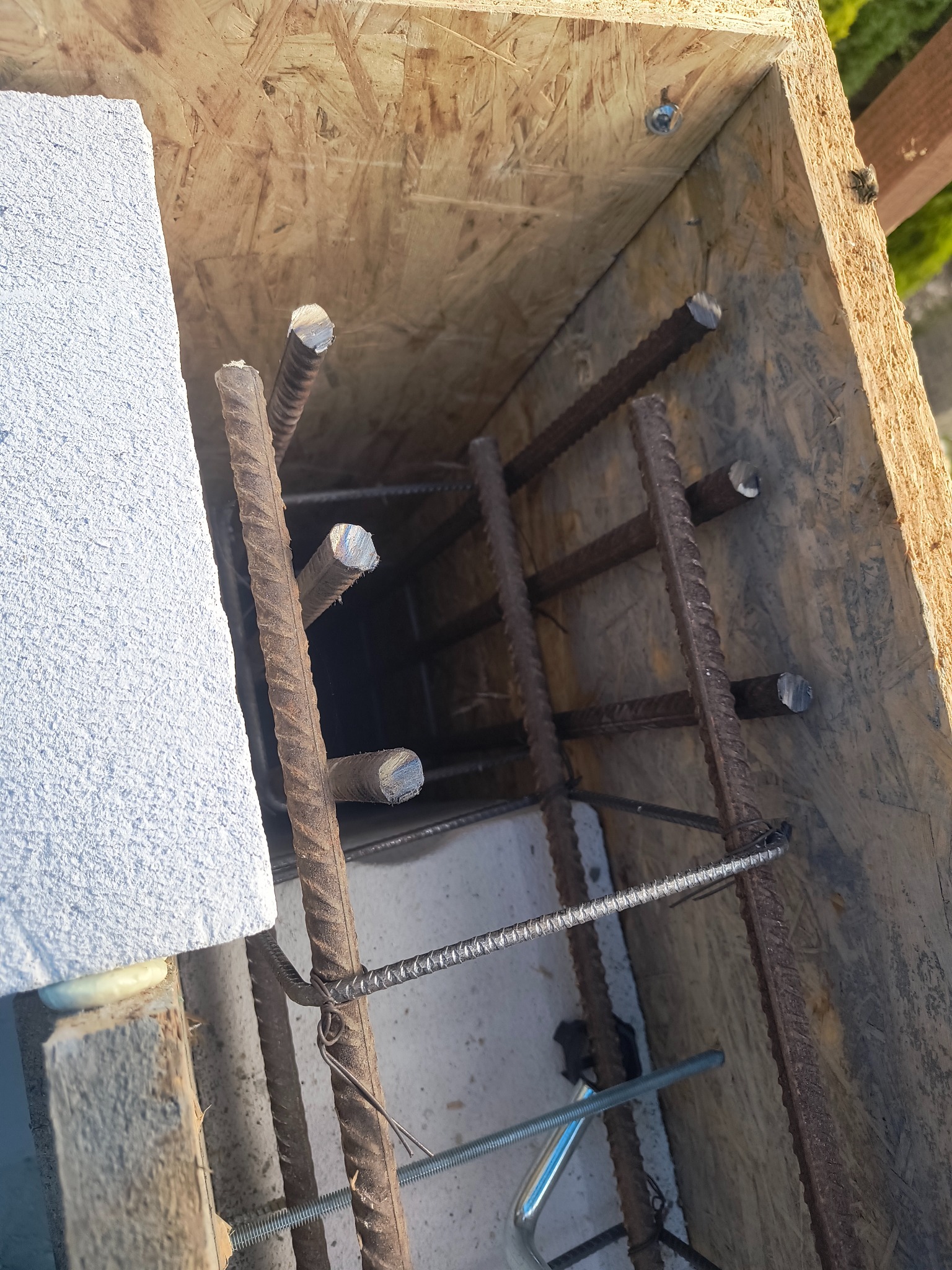 Zbrojenie pionowe w szalunku z płyty OSB, widok z góry. Element konstrukcyjny fundamentu, zbrojony pręt żebrowany, przygotowany do zalania betonem.