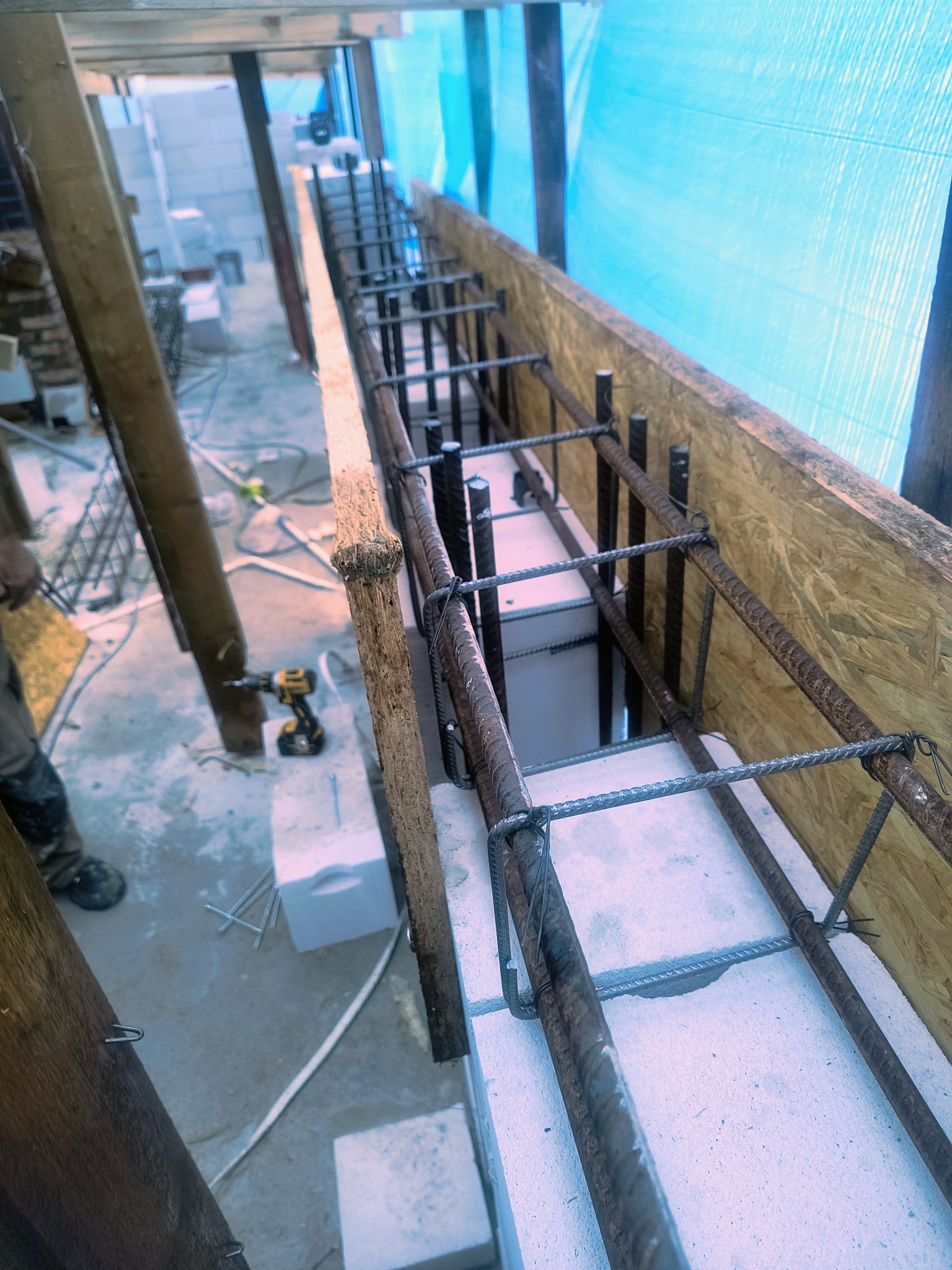 Zbrojenie fundamentów z użyciem bloczków betonowych i stalowych prętów, widoczne szalunki z desek i narzędzia budowlane. Etap budowy domu.