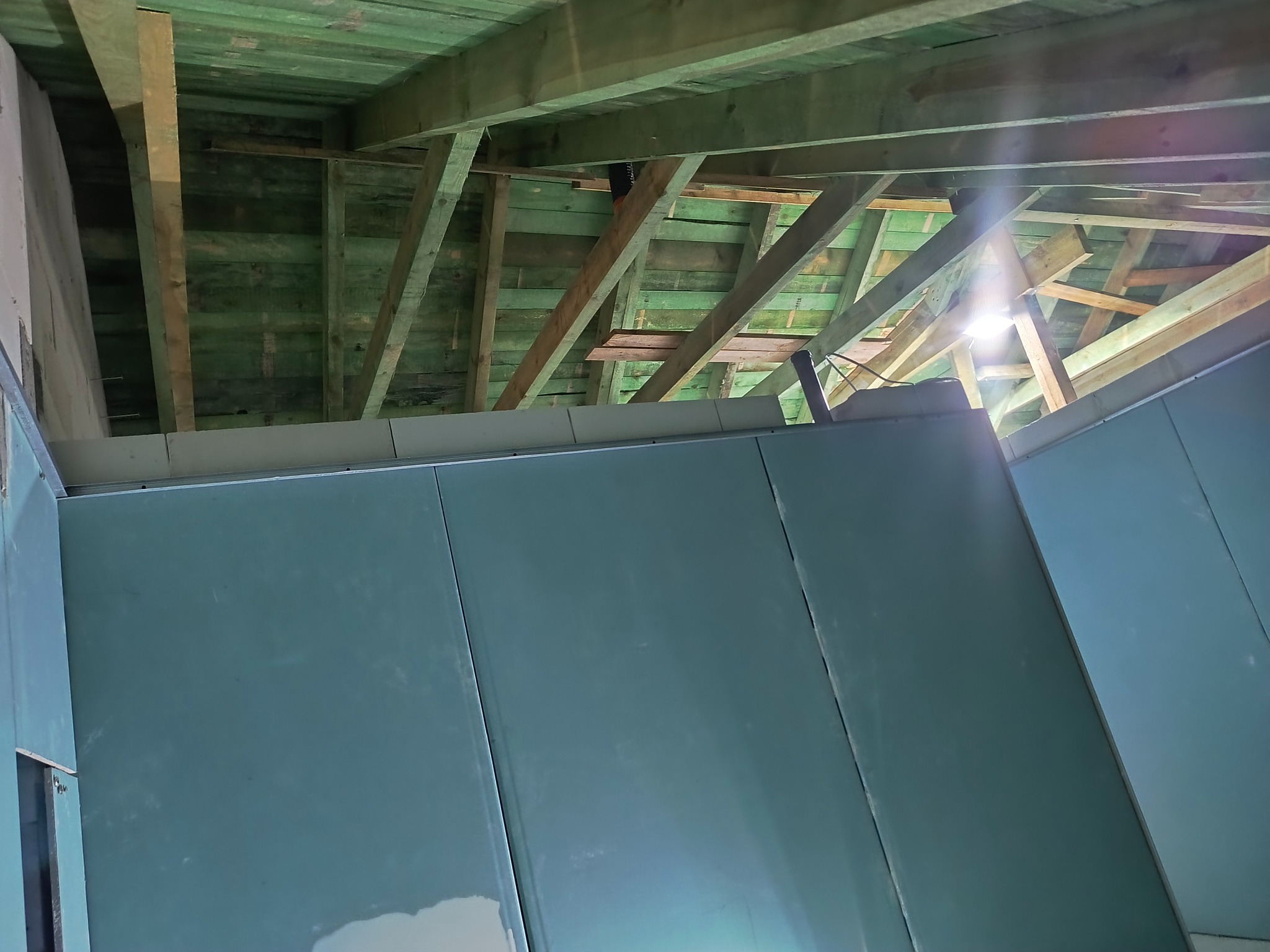 Montaż płyty karton gips na poddaszu z widoczną drewnianą konstrukcją dachu i oświetleniem. Prace wykończeniowe w trakcie realizacji.