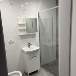 PRZEMYSŁAW DZIEDZIC PEPWO - Nowoczesna łazienka z białą armaturą i szklaną kabiną prysznicową. Widoczne niedokończone prace elektryczne przy suficie.