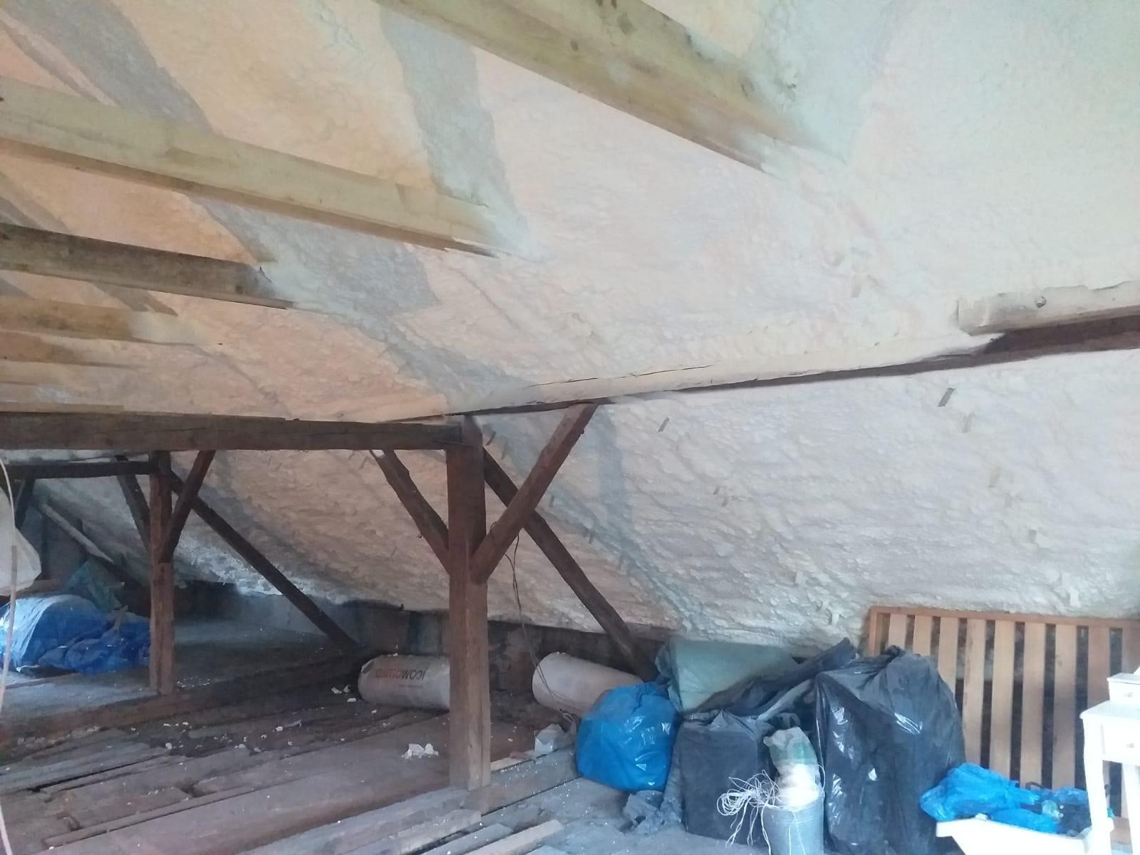 Poddasze z drewnianą konstrukcją i ociepleniem pianką PUR, widoczne worki i paleta. Realizacja ocieplenia natryskowego, detal drewnianych belek.