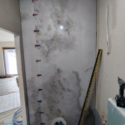 Flizenlega - Ściana z płytek imitujących marmur w trakcie montażu, z użyciem klipsów poziomujących. W tle widoczne narzędzia i przygotowane podłoże.