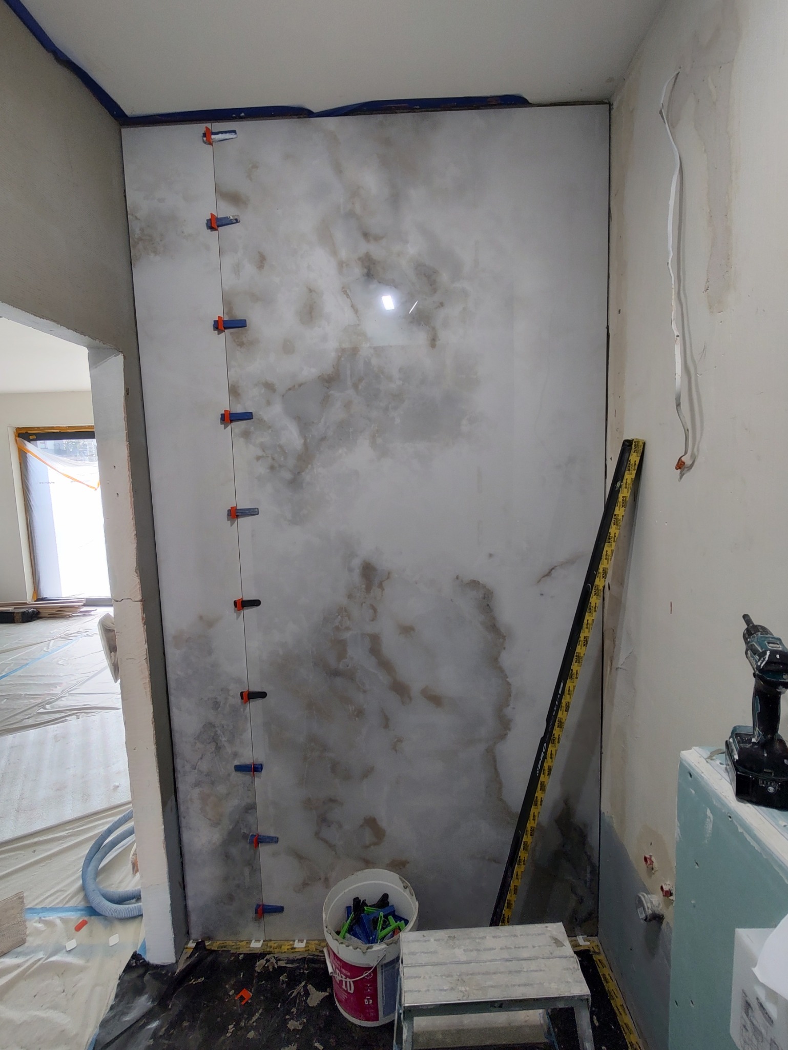 Ściana z płytek imitujących marmur w trakcie montażu, z użyciem klipsów poziomujących. W tle widoczne narzędzia i przygotowane podłoże.