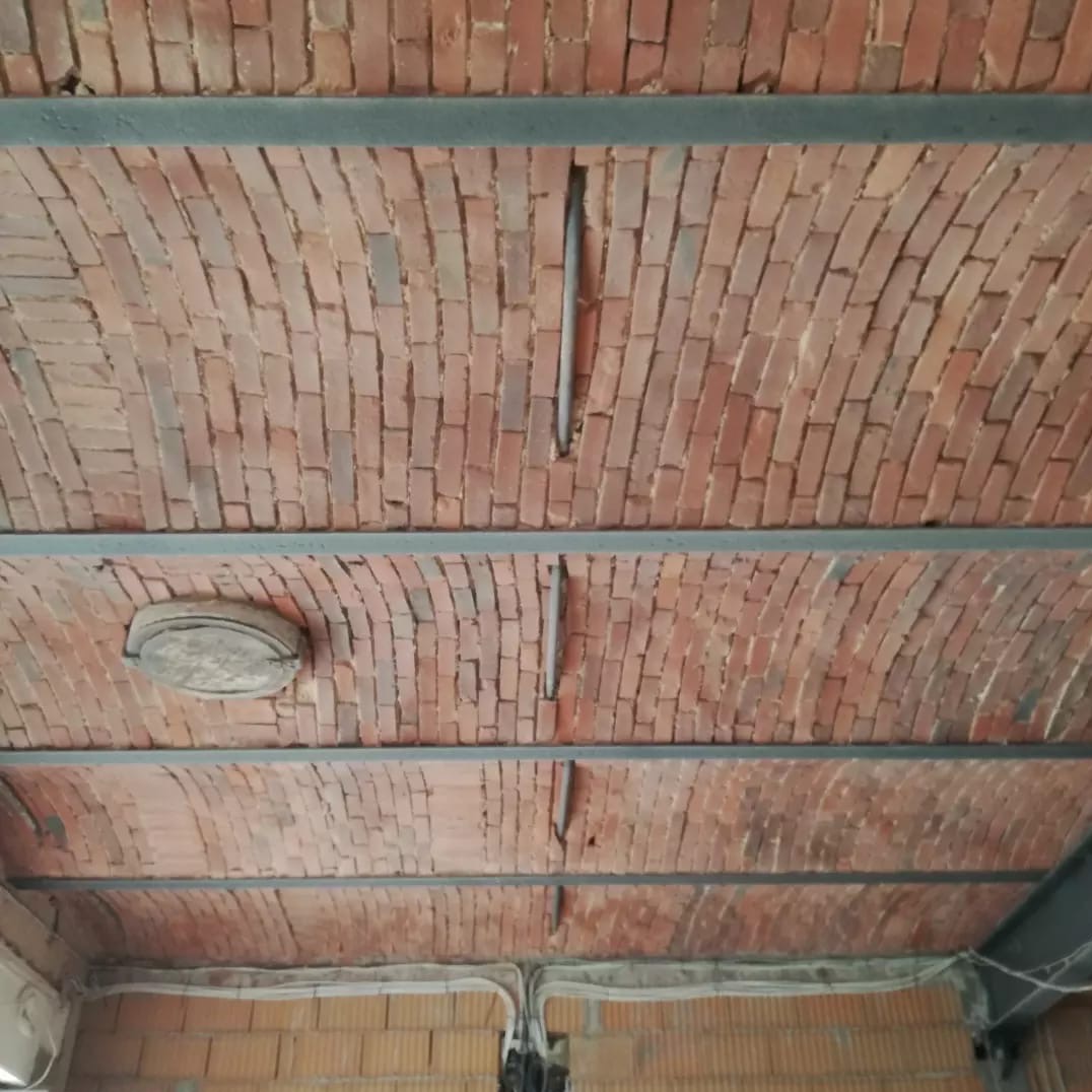 Ceglane sklepienie łukowe z widocznymi elementami konstrukcyjnymi i przewodami elektrycznymi. Nietypowe wykończenie sufitu z cegły klinkierowej.