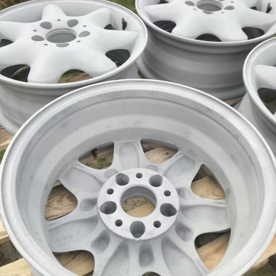 Białe felgi samochodowe po renowacji, ułożone na drewnianej palecie. Widoczne detale konstrukcji felg i równomierne pokrycie farbą. Cztery felgi w kadrze.