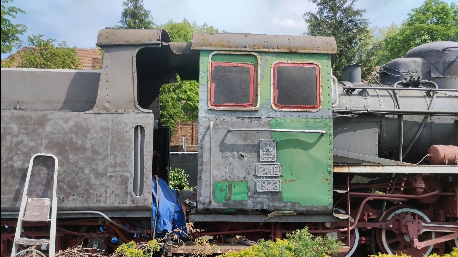 Lokomotywa PX48 z 1923 roku, w trakcie renowacji, z widocznymi śladami rdzy i odchodzącej farby, częściowo osłonięta folią. Widoczne detale konstrukcyjne.