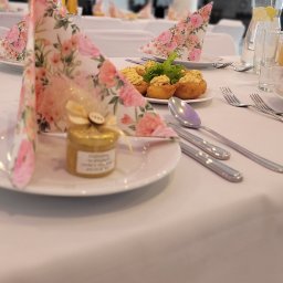 Zora Sp. Z o.o. - Udekorowany stół na przyjęcie: kanapki, serwetki w kwiaty, upominek dla gości w słoiczku. Elegancka aranżacja stołu z dbałością o detale i estetykę.
