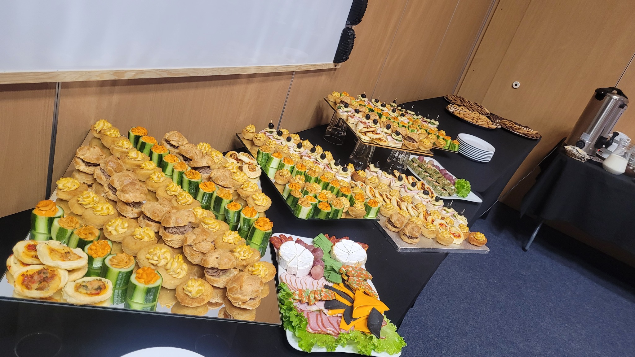 Stół cateringowy z różnorodnymi przekąskami: mini kanapeczki, koreczki, sałatki, sery i wędliny. Elegancka prezentacja, idealna na firmowe przyjęcie.