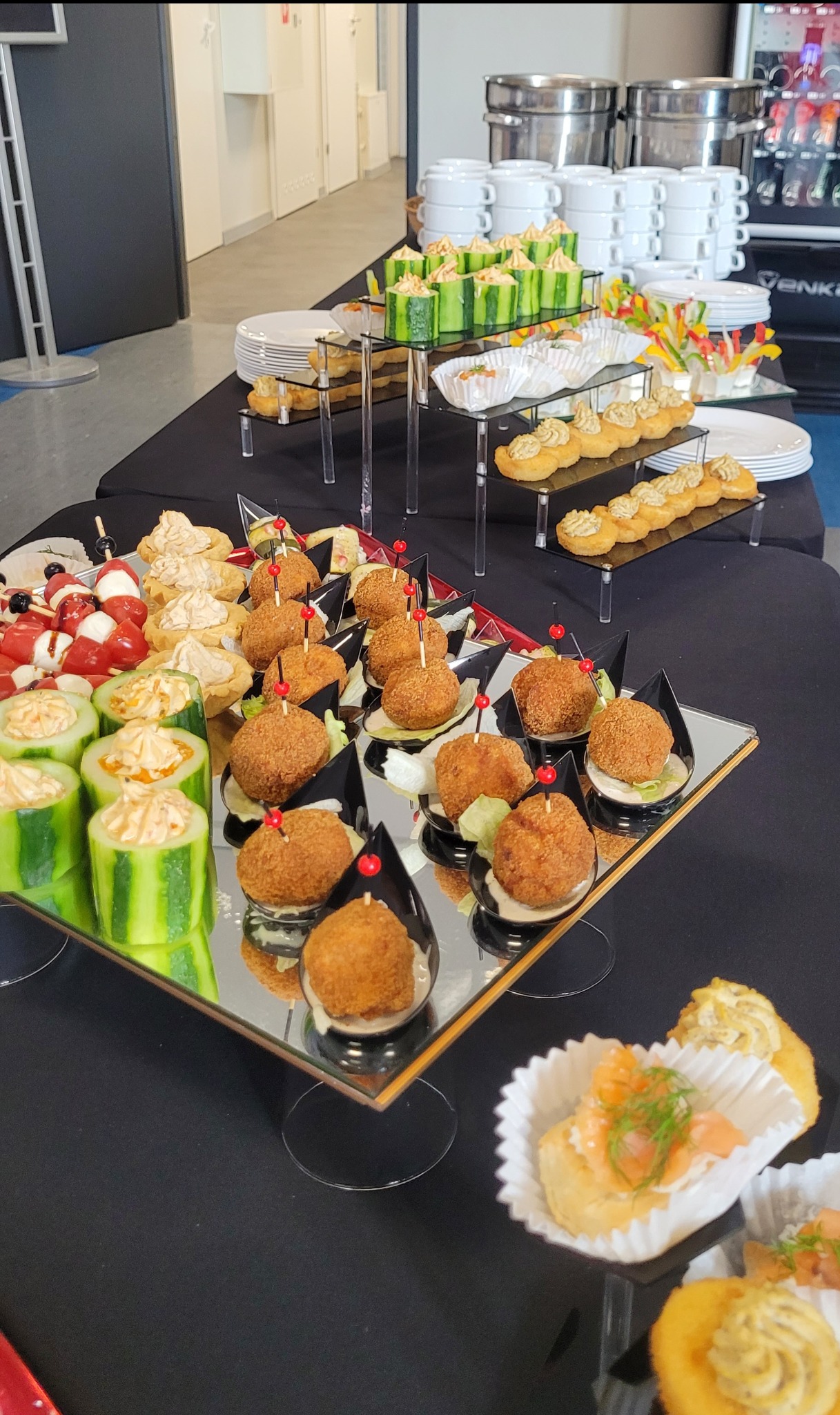 Elegancko przygotowany stół cateringowy z różnorodnymi przekąskami, w tym kulkami mięsnymi, tartaletkami i ogórkami z nadzieniem, na czarnym obrusie.