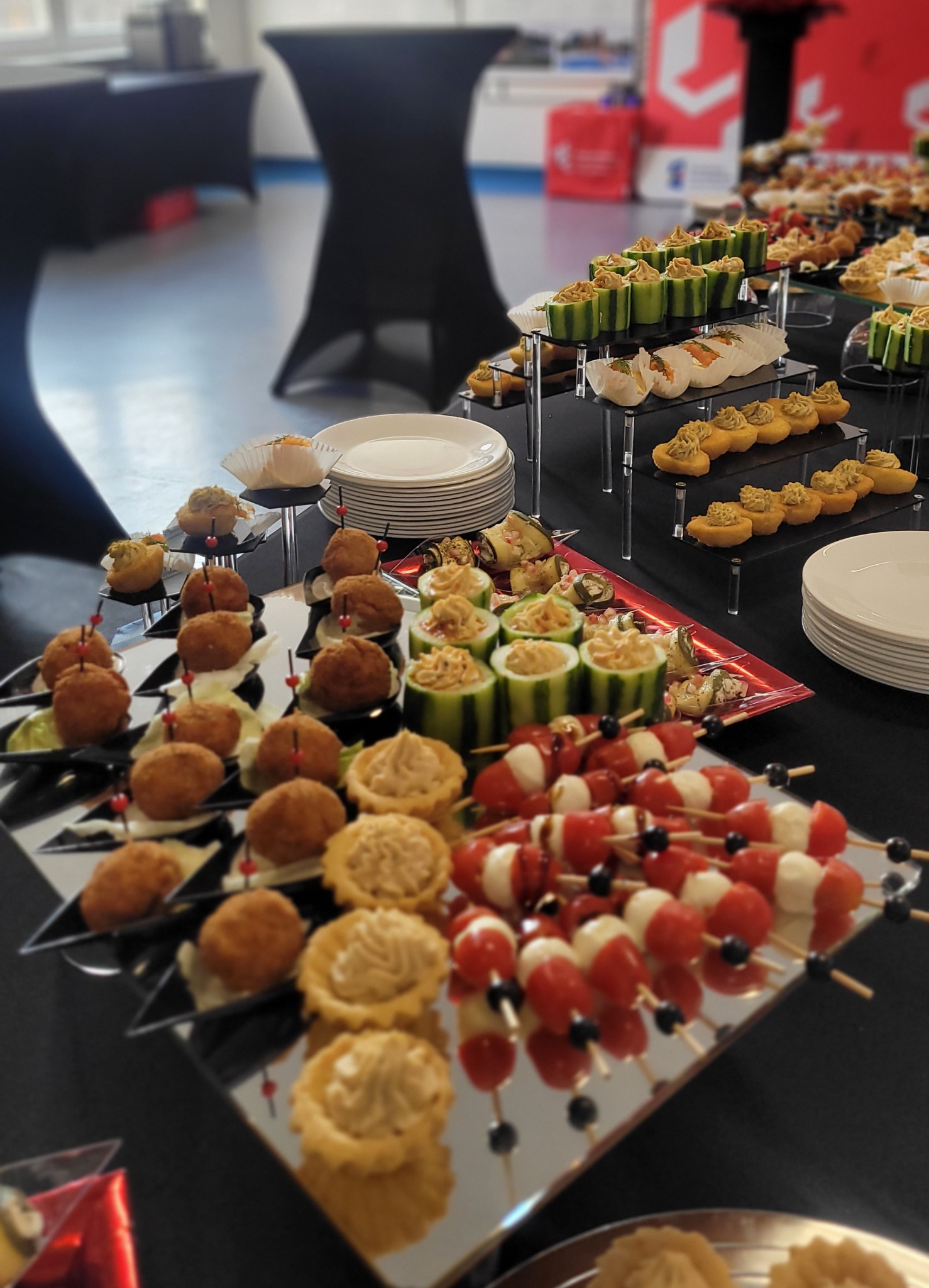 Stół cateringowy z różnorodnymi przekąskami: koreczki caprese, tartaletki, jajka faszerowane i ogórki z pastą. Profesjonalna aranżacja na czarnym obrusie.