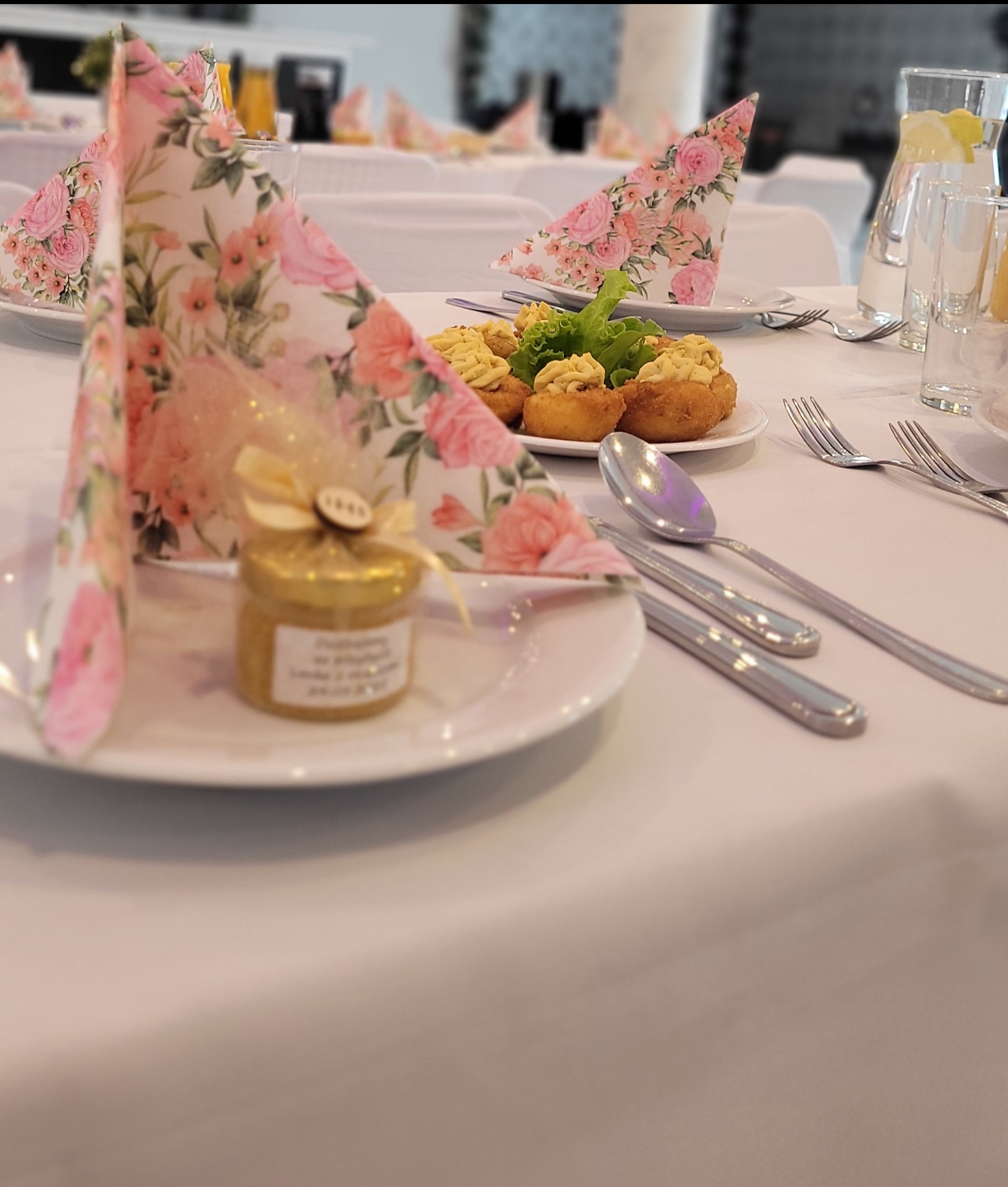 Udekorowany stół na przyjęcie: kanapki, serwetki w kwiaty, upominek dla gości w słoiczku. Elegancka aranżacja stołu z dbałością o detale i estetykę.