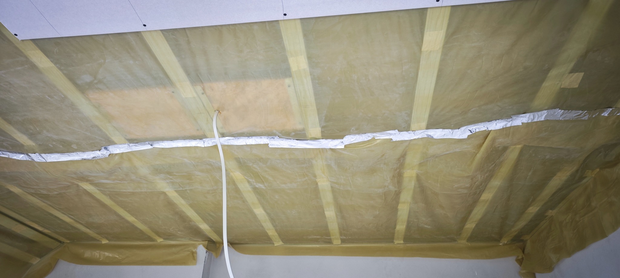 Folia paroizolacyjna na drewnianej konstrukcji poddasza, zabezpieczona taśmą aluminiową, przygotowana do montażu płyt karton-gips.