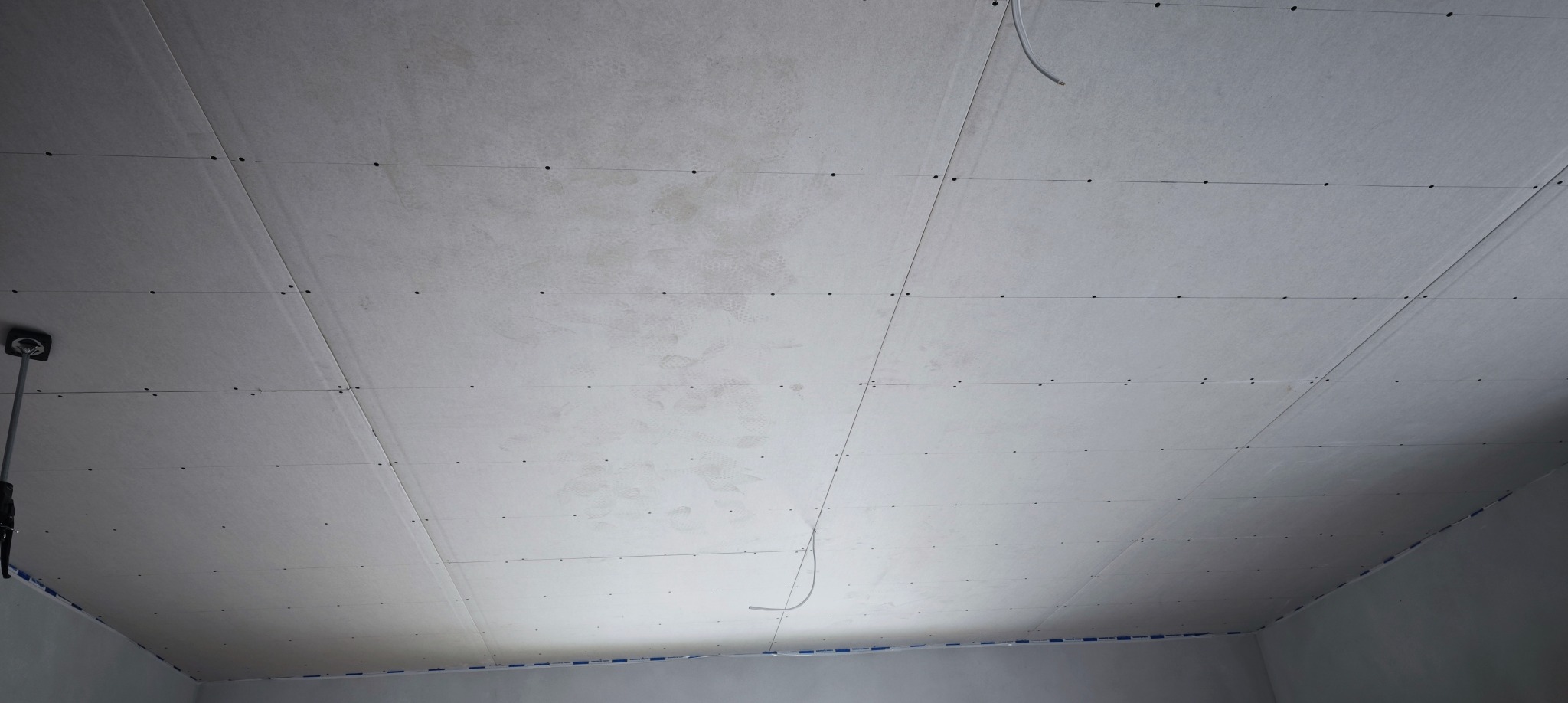 Sufit z płyt kartonowo-gipsowych, widoczne łączenia i śruby montażowe, częściowo widoczne przewody elektryczne, przygotowany do dalszych prac wykończeniowych.