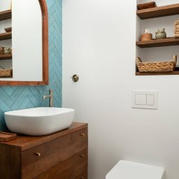 PRE-LOVED - Nowoczesna łazienka z umywalką nablatową na drewnianej komodzie, błękitnymi płytkami ułożonymi w jodełkę i drewnianymi półkami wnękowymi.