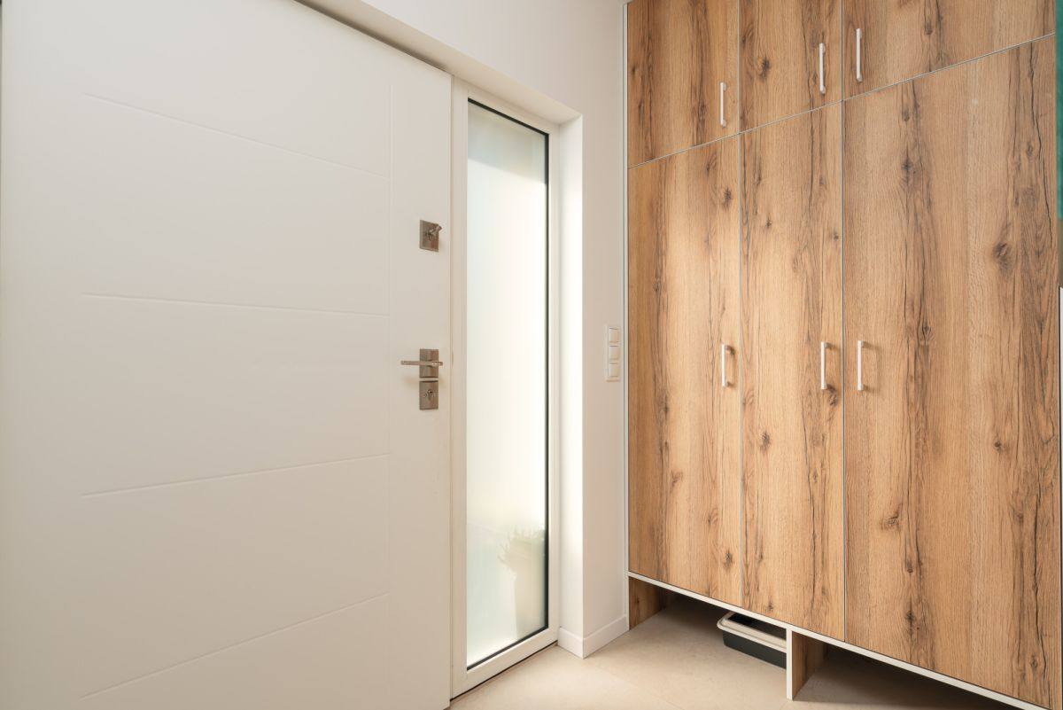 Nowoczesne wnętrze: białe drzwi z szybą i drewniana szafa w zabudowie. Minimalistyczny design, jasne kolory, widoczne detale wykończenia.