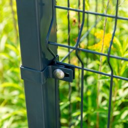 Palisada.pl - Szczegółowy widok na mocowanie panelu ogrodzeniowego do słupka. Widoczne elementy złączne i fragment siatki na tle zieleni.