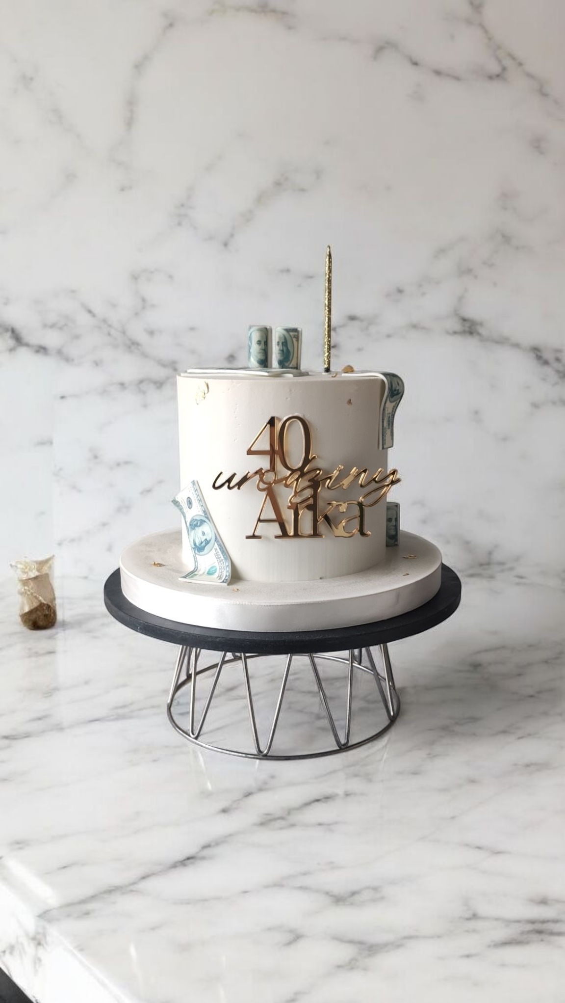 Tort urodzinowy w stylu glamour: biały krem, złote napisy '40 Urodziny Alka', dekoracja z imitacji banknotów na marmurowym tle.