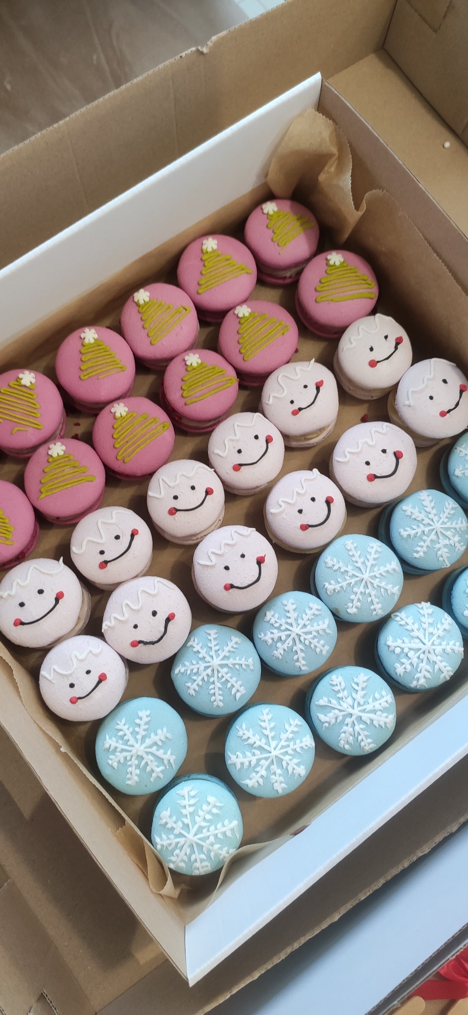 Świąteczne makaroniki w pudełku z motywami choinek, uśmiechniętych buziek i śnieżynek, przygotowane w cukierni w Pyrzycach. Różowe, białe i błękitne.