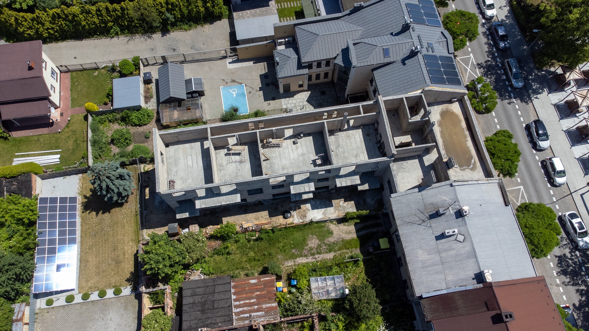 Zdjęcie z drona ukazuje stan surowy dwukondygnacyjnego budynku z betonu komórkowego. Widoczny plac budowy, fragmenty dachu z panelami solarnymi i sąsiednia zabudowa.