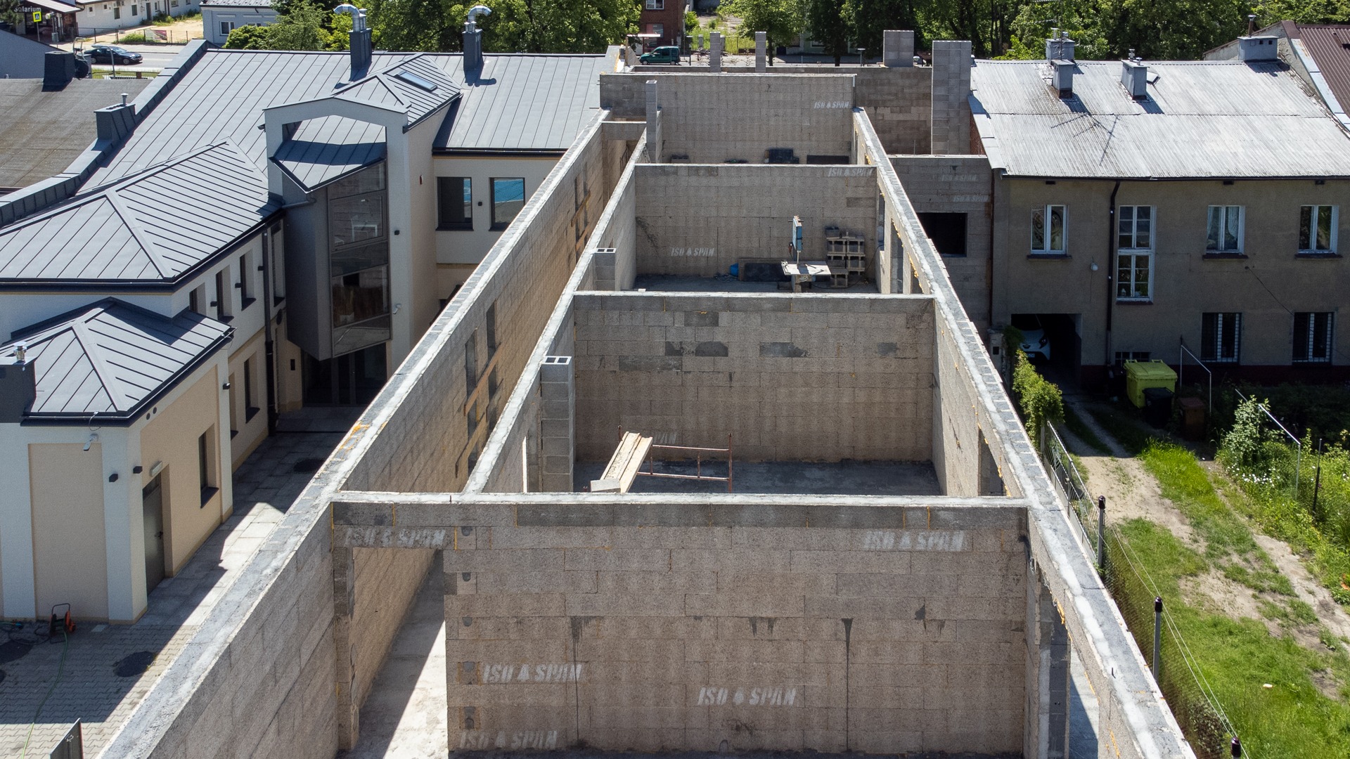 Wysoka perspektywa na budowę domu z bloczków betonowych ISO SPAN, widoczne ściany parteru i sąsiednie budynki. Etap murowania ścian.