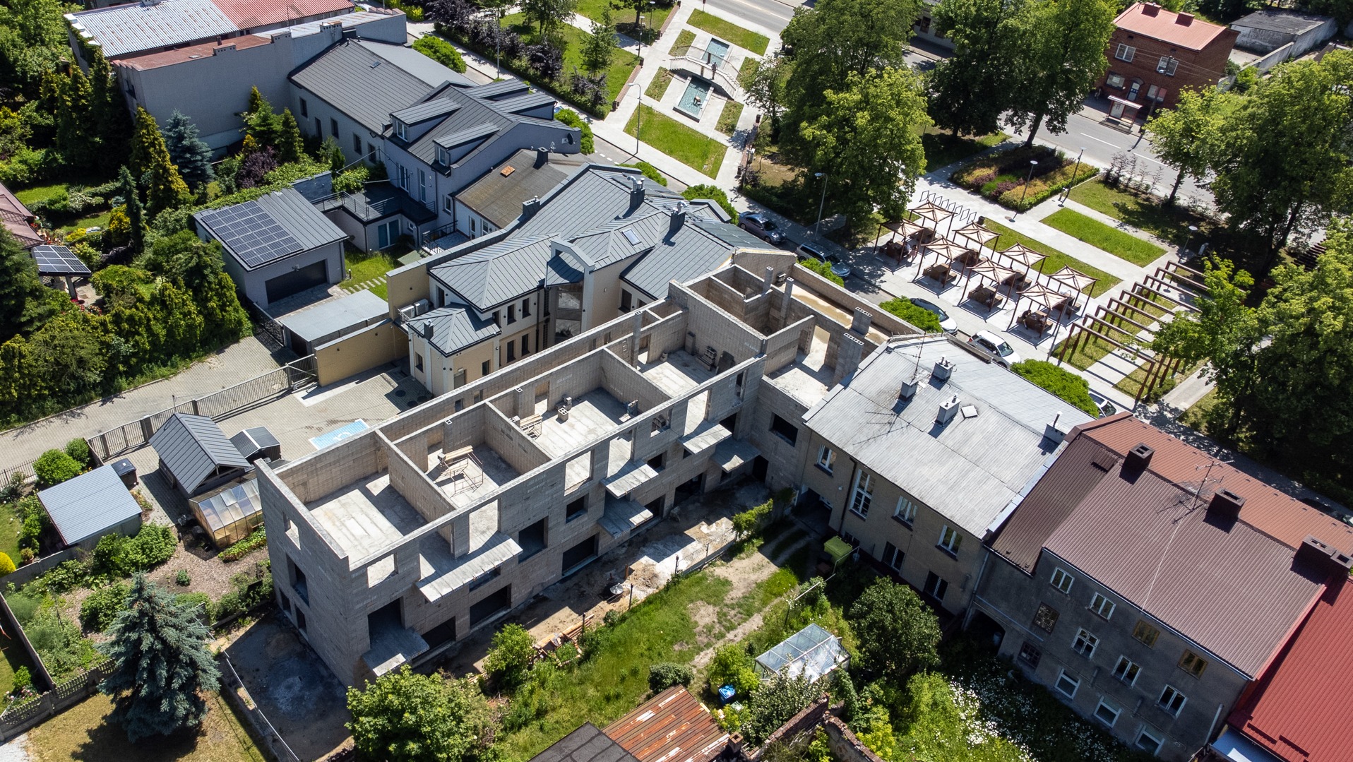 Zdjęcie z lotu ptaka przedstawia budynek w trakcie murowania ścian, z widocznymi elementami konstrukcyjnymi i otaczającą zielenią.