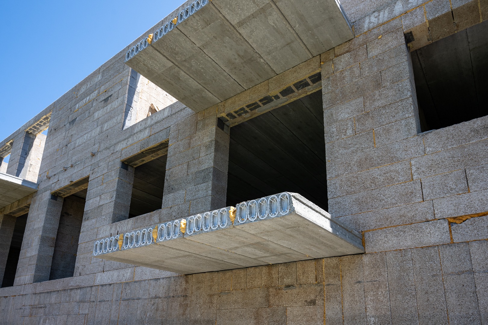 Wznoszenie surowego, dwukondygnacyjnego domu z betonu komórkowego. Widoczne otwory okienne i strop z prefabrykatów. Żółta pianka uszczelniająca w spoinach.