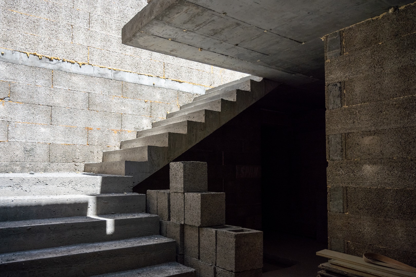 Surowe, betonowe schody w trakcie budowy domu z bloczków, z widocznymi spoinami wypełnionymi pianką montażową i stosem bloczków obok schodów.