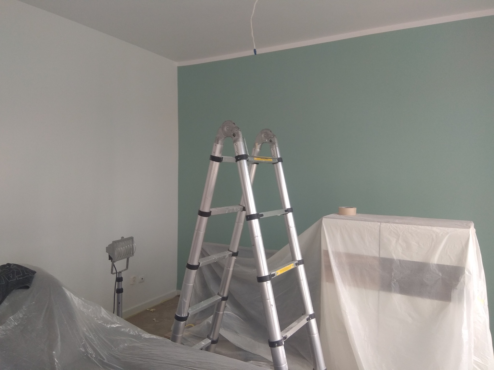 Pokój po odświeżeniu barw, ściana w odcieniach zieleni, drabina malarska i zabezpieczone meble folią w Elblągu.