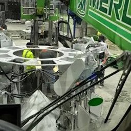 Remtech pro - Wnętrze hali: widok z kabiny dźwigu na konstrukcję stalową z pracownikami w żółtych kamizelkach. Dźwig marki Merlo w trakcie pracy.