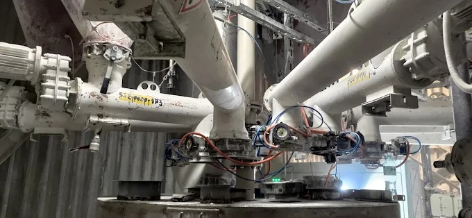 Kompleksowy system rurociągów przemysłowych, pomalowany na biało, z licznymi zaworami i przyłączami, tworzący rozbudowaną instalację w hali produkcyjnej.