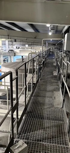 Wnętrze hali produkcyjnej w Bogumiłowie z metalowymi zbiornikami i kratownicową kładką. Widoczne elementy konstrukcji stalowej i oświetlenie przemysłowe.