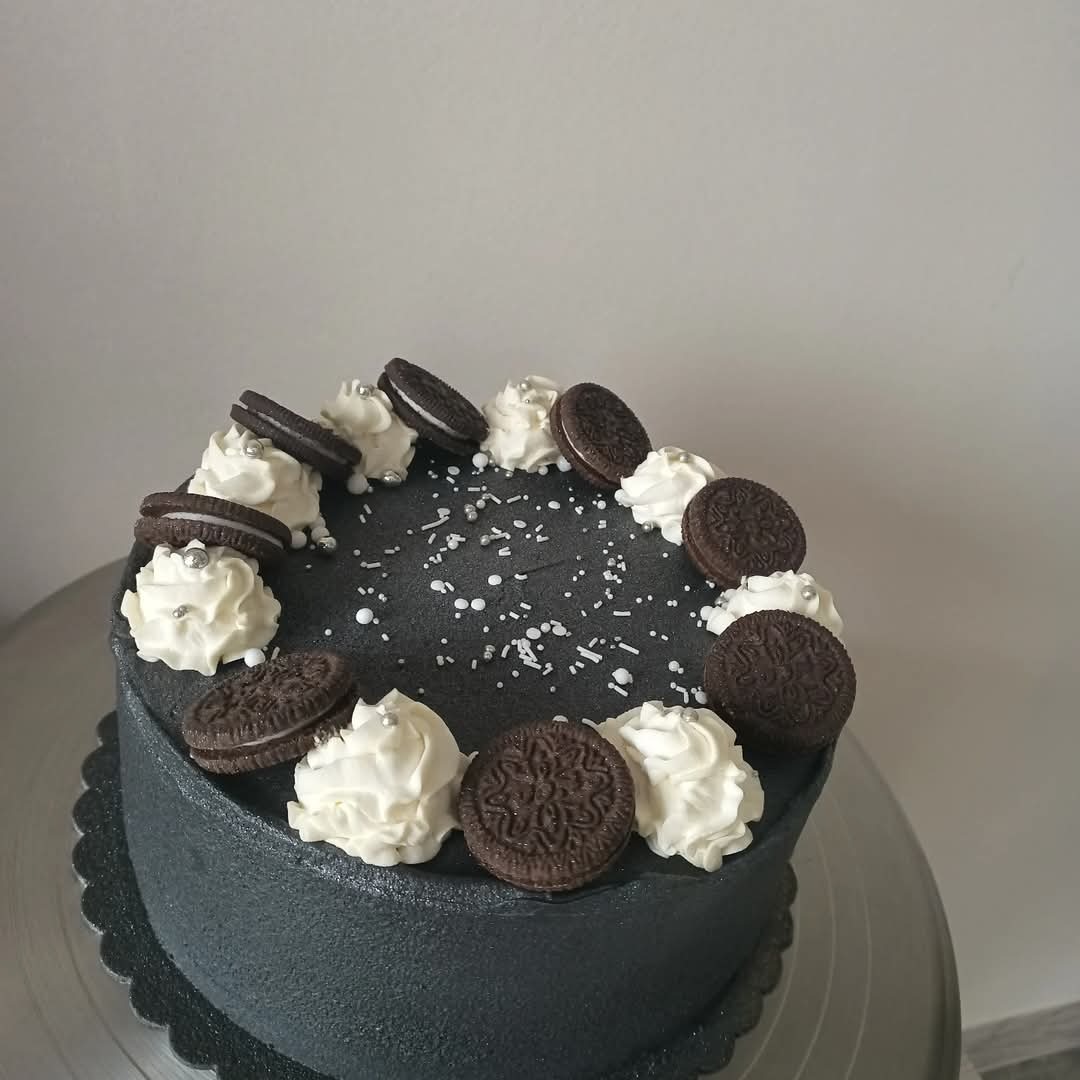 Ciemny tort zdobiony kremem, ciasteczkami Oreo i srebrnymi kuleczkami, na metalowej paterze, z bliska, z boku, na jasnym tle. Minimalistyczny design.