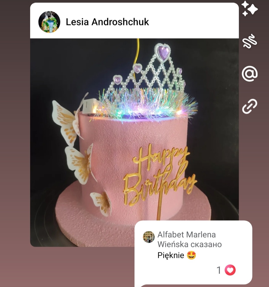 Różowy tort urodzinowy z koroną i motylami, zdobiony napisem 'Happy Birthday' w złotym kolorze, oświetlony diodami, na ciemnym tle.